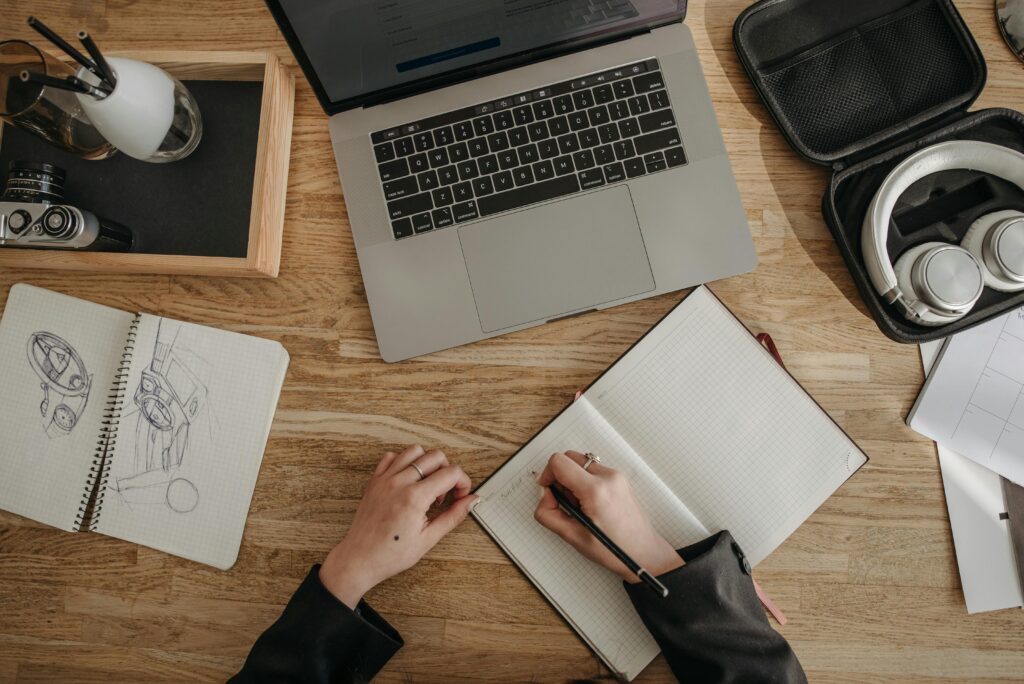 Top view of a creative workspace featuring a laptop, sketchbooks, and headphones on a wooden desk.
